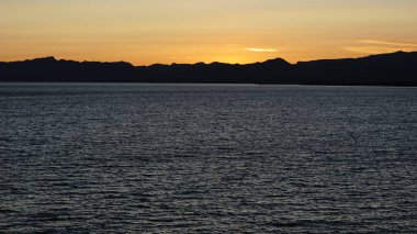 Gün batımında deniz dağ siluetine karşı