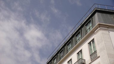 Modern bir binanın köşesi yumuşak, bulutlu bir gökyüzüne karşı yükselir. Temiz çizgiler, sessiz tonlar ve simetri minimalist mimari çalışmaları.