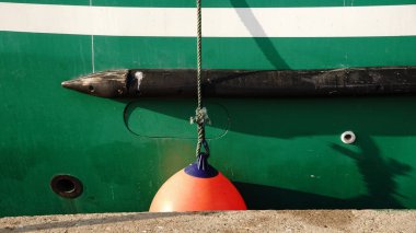 Close-up of an orange buoy tied with a rope to a green boat hull with black and white details.