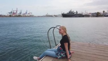 Ahşap iskelede oturan, denize bakan bir kadın özgür hissediyor, deniz mavisi su ve gökyüzünün arka planı..