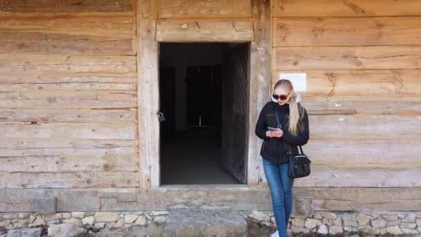 Žena používající mobilní telefon v blízkosti dřevěného domu ve staré vesnici. — Stock video