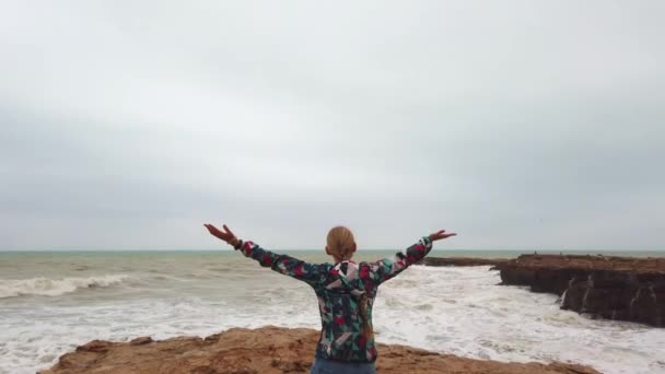 Девушка поднимает руки, стоя спиной к берегу моря во время шторма. — стоковое видео