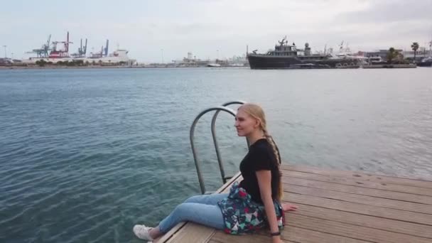 Ahşap iskelede oturan, denize bakan bir kadın özgür hissediyor, deniz mavisi su ve gökyüzünün arka planı.. — Stok video