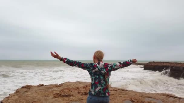 Schöne Mädchen auf dem Meer im Sturm. Mädchen blickt in die Ferne auf das Meer. Meereswellen brechen an der Küste. — Stockvideo