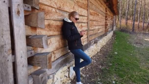 Donna che utilizza smart phone vicino a una casa in legno in un vecchio villaggio. — Video Stock