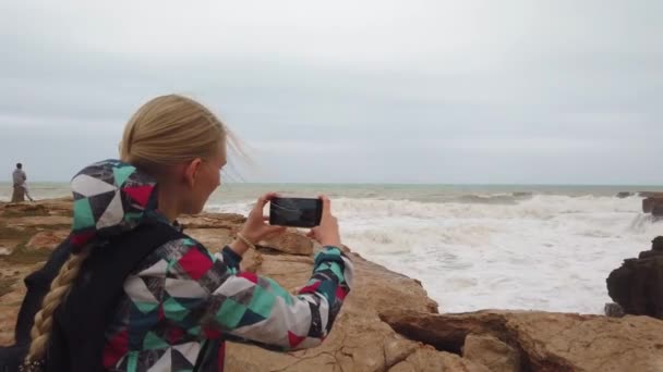 Kız sırtüstü duruyor ve cep telefonuyla deniz kenarında fotoğraf çekiyor. Yavaş çekim — Stok video