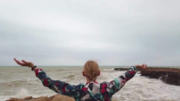 Chica levanta las manos mientras está de pie con su espalda en la orilla del mar durante una tormenta . — Vídeo de stock