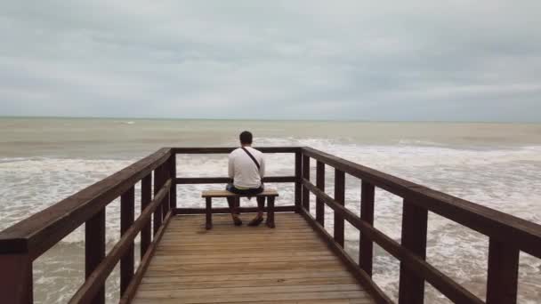 Мужчина сидит на скамейке и смотрит на шторм. — стоковое видео