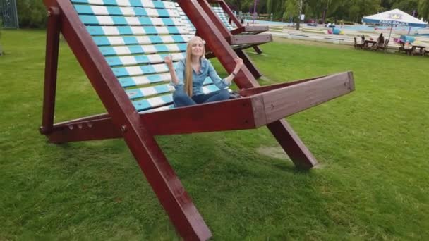 A menina meditando em uma cadeira de praia muito grande no parque . — Vídeo de Stock