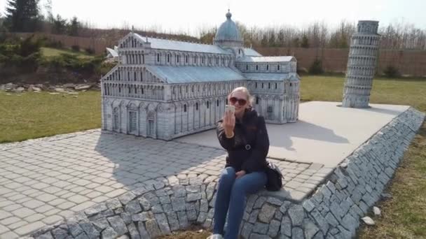 Mulher tira uma selfie perto de um modelo em miniatura da antiga Catedral, Europa. Parque de Miniaturas . — Vídeo de Stock