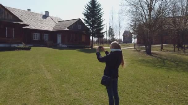 Woman tourist makes a photos of wooden house in an old European village — Stock Video