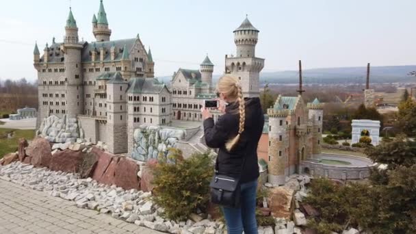 Neuschwanstein, Almanya 'daki eski şatonun minyatür bir maketinin yanında yürürken kadın fotoğraf çekiyor. Minyatürler Parkı. — Stok video