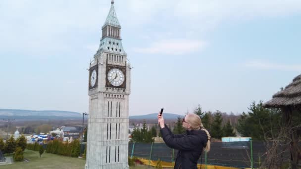 Kadın, Londra 'daki Big Ben Kulesi' nin minyatür bir maketinin yanında yürürken fotoğraf çekiyor. Minyatürler Parkı. — Stok video