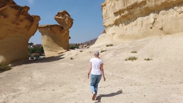Девушка, идущая по пустыне рядом с желтой футуристической скалой. — стоковое видео