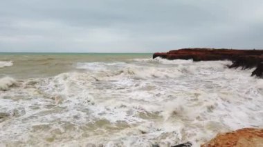 Büyük dalgalar kayalık sahilde kırılır, beyaz köpük suda..