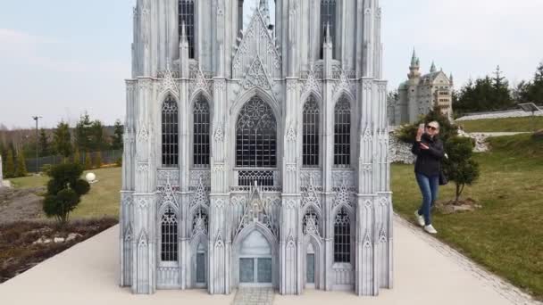 在欧洲一个古老的大教堂的缩影模型附近，一个女人正在步行拍照。小型公园. — 图库视频影像