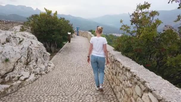 Blond flicka går på defensiv väggar medeltida slott i Europa berg. — Stockvideo