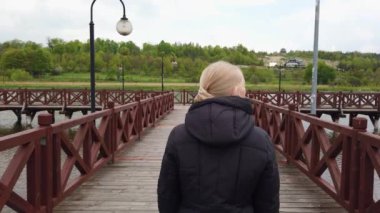 Sarışın kız köprüde yürüyor ve kameraya bakıyor..