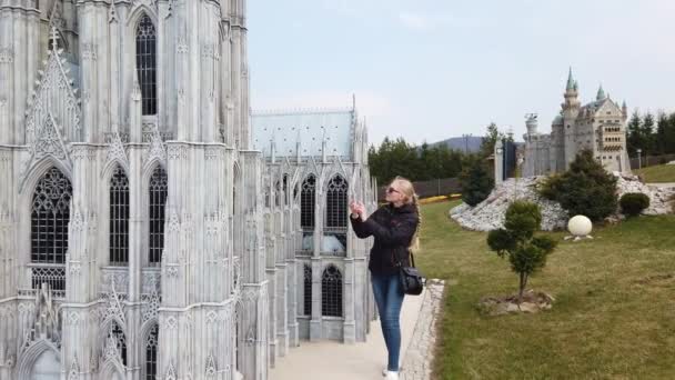 在欧洲一个古老的大教堂的缩影模型附近，一个女人正在步行拍照。小型公园. — 图库视频影像