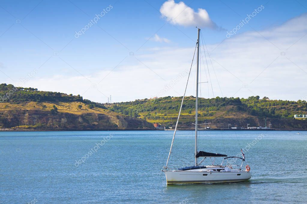 Sailboat with lowered sails is crossing the portuguese Tejo river (Portugal)