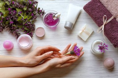 Klasik beyaz bir arka planda kadın eli. Kremler, önlükler, sabunlar, mumlar, arka planda bir havlu. El bakımı. Doğal ve organik kozmetik ürünleri. Boya ya da kimyasallar yok. El hijyeni.