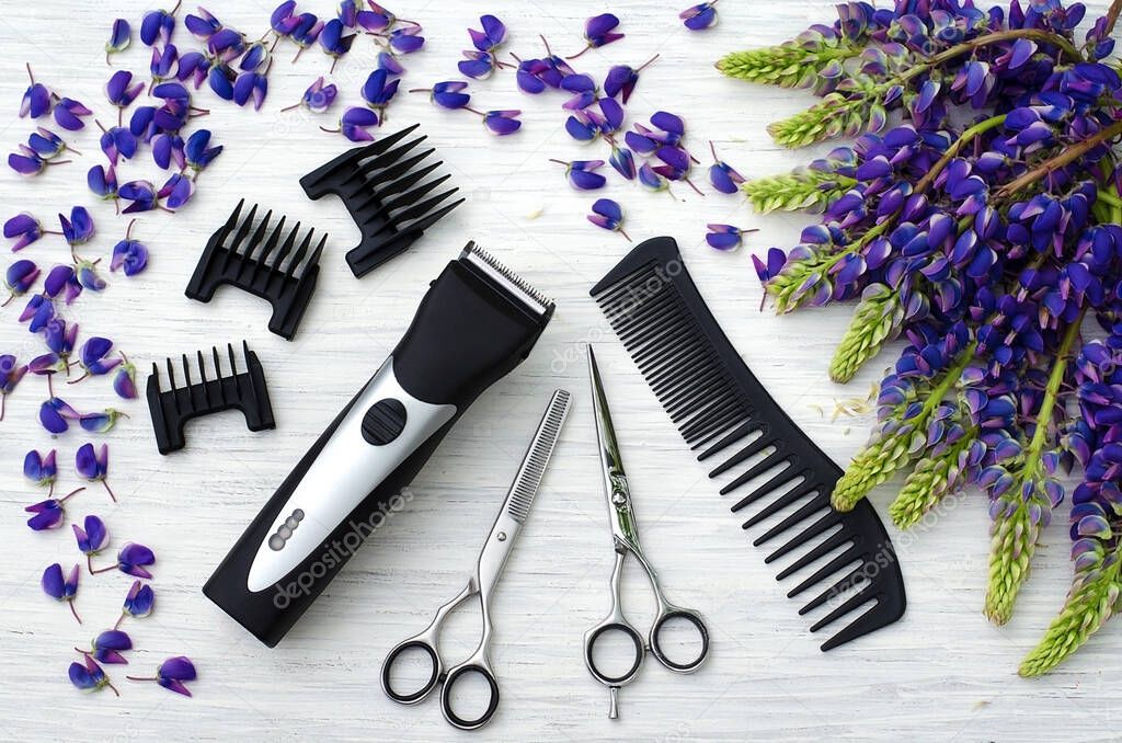 Barber machine, scissors for haircuts, nozzles for haircuts, comb on a white wooden background.Purple with Green Lupine. Hairdressing tools on a background of bright purple flowers. 