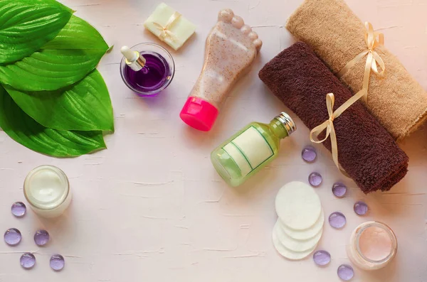 Green fresh leaves on the background of organic cosmetics. Towels, cotton pads, pink cream, green gel, handcrafted soap, natural, foot care, pedicure, healthy feet