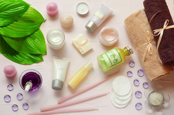 Green fresh leaves on the background of organic cosmetics. Towels, cotton pads, pink cream, green gel, candle soap. Natural cosmetics. SPA. Aromatherapy.Flat view