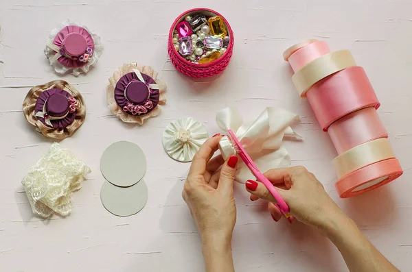 9. adım. Beyaz bir masada pembe makas, kumaş, mücevher, kurdele ve tokalar var. El işi yapan kadın eller tasvir edilir. Kendi ellerinizle. Adım adım talimat. Diy. Yeni yıl için el sanatları