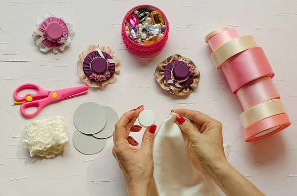 9. adım. Beyaz bir masada pembe makas, kumaş, mücevher, kurdele ve tokalar var. El işi yapan kadın eller tasvir edilir. Kendi ellerinizle. Adım adım talimat. Diy. Yeni yıl için el sanatları