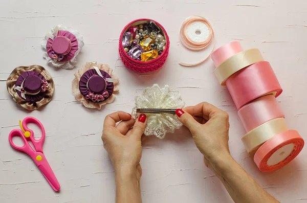 9. adım. Beyaz bir masada pembe makas, kumaş, mücevher, kurdele ve tokalar var. El işi yapan kadın eller tasvir edilir. Kendi ellerinizle. Adım adım talimat. Diy. Yeni yıl için el sanatları