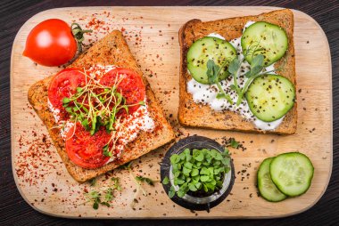 Krem peynirli sağlıklı sandviçler, mikroyeşiller, salatalık dilimleri ve iki kiraz domatesli baharatlar ve fesleğenli mikroyeşil lahanalı küçük kavanoz. Sağlıklı beslenme, diyet vejetaryen yemekleri..