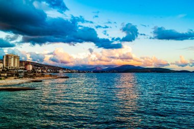 Arnavutluk 'un kıyı şeridi boyunca yer alan Saranda kasabasının akşam manzarası. Güzel bir akşam gökyüzü, gün batımı. Güney Arnavutluk 'taki İyon denizi, turizm beldesi.