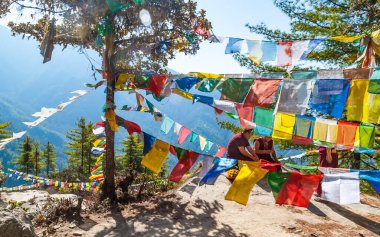 Paro, Butan - Şubat 2016: Geleneksel kırmızı elbiseli Budist keşiş ve Himalayalar 'daki Tibet Budist bayrakları Lung Ta Taktsang Manastırı ya da Kaplan Yuvası yolunda