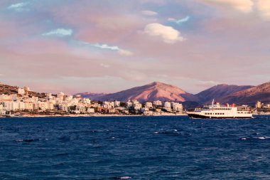 Arnavutluk 'un Saranda körfezindeki küçük feribot Arnavutluk dağlarının arka planında. Gün batımı, bulutlu gökyüzü.