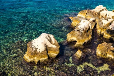 Açık deniz suyu dalgaları ve Arnavutluk 'un güneyindeki deniz kıyısında büyük bir taş. Güzel turkuaz deniz suyu. Deniz suyu yüzeyinde güneş yansıması.