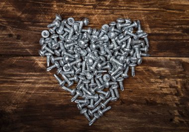 Eski kahverengi tahta üzerinde gümüş renkli vidalardan yapılmış kalp şeklinde bir figür. Metalik yapay kalp makinesi, robot, mekanizma, Sevgililer Günü, güçlü sonsuz aşk kavramı.