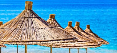 Mavi turkuaz bir arka planda sazlık plaj şemsiyelerine yakın çekim. Tropik tatil köyü yaz arkaplanı. İnsan yok. Boş metin alanı.