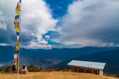 Geleneksel Tibet Budist bayrakları Lung Ta ve Bhutan 'daki Himalaya dağlarındaki Phajoding Manastırı' nın küçük ev binası. Thimphu Vadisi manzarası. Mavi gökyüzünde beyaz bulutlar.