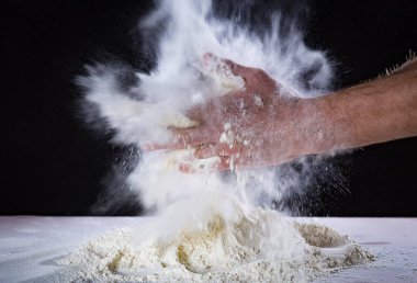 Şef insanın ellerini kapatın. Masadaki hamuru un ile yoğurmaya hazırlanın. Fırında ya da evde elle para kazanıyordum. Un bulutu havada. Siyah arkaplan.