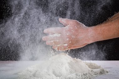 Şef insanın ellerini kapatın. Masadaki hamuru un ile yoğurmaya hazırlanın. Fırında ya da evde elle para kazanıyordum. Un bulutu havada. Siyah arkaplan.