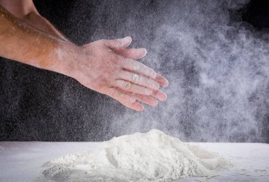 Şef insanın ellerini kapatın. Masadaki hamuru un ile yoğurmaya hazırlanın. Fırında ya da evde elle para kazanıyordum. Un bulutu havada. Siyah arkaplan.