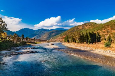 Mo Chhu Nehri güneşli bir günde, Punakha, Butan. Punakha Dzong yakınlarındaki tahta kantilever köprüsünden nehre Punakha şehrinin ve Himalaya dağlarının evlerinin manzarası.