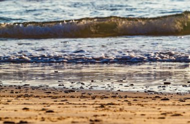 Gün batımında kumsala yakın kum ve deniz dalgası. Güneş sakin sahile yansıyor. Yumuşak odaklanma. Yaz tatili geçmişi.