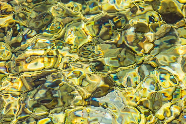 Abstract background of clear sea or river water ripple waves in light green khaki color. Sea water with different color pebbles at the bottom. Sun reflection on sea water surface.