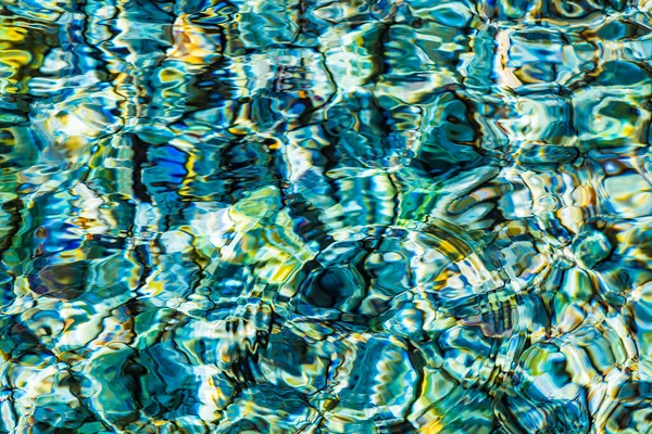 Abstract background of clear sea or river water ripple waves in blue, green, yellow color. Sea water with different color pebbles at the bottom. Sun reflection on sea water surface.