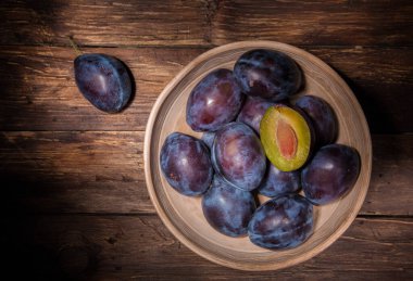 Koyu ahşap tahtanın üzerinde erikli seramik kase. Meyve arkaplanı. Üst Manzara. Tarım, Bahçe, Hasat Konsepti.