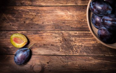 Erikli seramik kase ve koyu ahşap tahtanın üzerinde taşla birlikte bir buçuk erik. Meyve arkaplanı. Metin uzayı. Üst Manzara. Tarım, Bahçe, Hasat Konsepti.