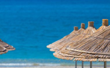 Turkuaz, sıcak deniz arka planında sazlık plaj şemsiyelerinin yakın çekimi. Metin uzayı.