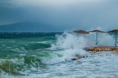 Güçlü fırtına, karanlık bulutlu gökyüzü, dalgalar ve deniz rüzgarı, dalgalar plaj şemsiyelerini sürükledi, yüzme ve sörf için tehlike